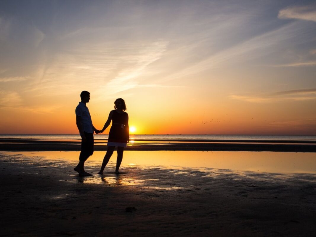 Couple walking hand in hand on Westward Ho! beach at sunset.